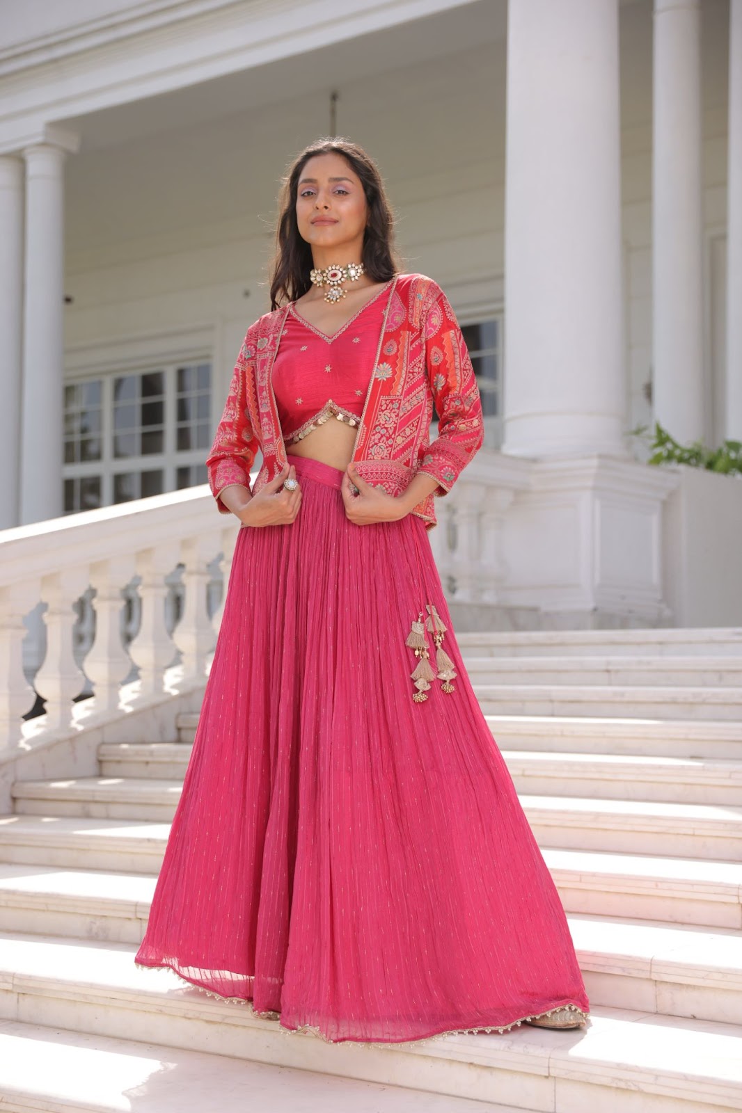 A model wearing indo-western pink coloured crop top lehenga with embroidered jacket.